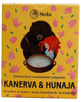 Solan Kanerva & Hunaja -saippua ihanassa keltapohjaisessa pahvipakkauksessa, jossa on piirrettynä pinkkejä kukkia, sekä karhu ja punatukkainen tyttö sekoittelemassa saippuapataa.