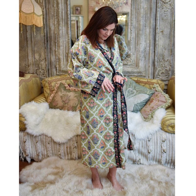 Tummahiuksinen nainen sitoo Powell Craftin vihreän, persikan ja tummansinisen sävyisen puuvilla-aamutakin vyötä.