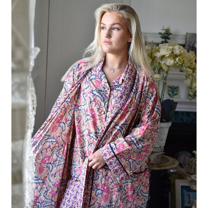 Powell Craftin kimono-aamutakki ja pyjama samalla kuosilla vaaleahiuksisen naisen yllä. Kuosissa on aprikoosinsävyisellä pohjalla laivastonsinisiä ja persianpunaisia kuvioita.