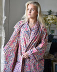 Powell Craftin kimono-aamutakki ja pyjama samalla kuosilla vaaleahiuksisen naisen yllä. Kuosissa on aprikoosinsävyisellä pohjalla laivastonsinisiä ja persianpunaisia kuvioita.
