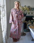 Powell Craftin Apricot, Navy & Persian Red Mixed Block Print -kuvioinen naisten kimono-aamutakki pitsiverhoisen ikkunan edessä poseeraavan naisen yllä.