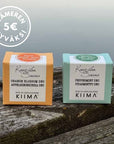 Kaksi Kaurilan sauna X KIIMA -deopalaa laiturinnokassa, tuoksuissa appelsiininkukka ja piparminttu. Vasemmassa yläkulmassa logo, jossa lukee "5€ Itämeren hyväksi", John Nurmisen säätiön kanssa tehtävään kampanjaan liittyen.