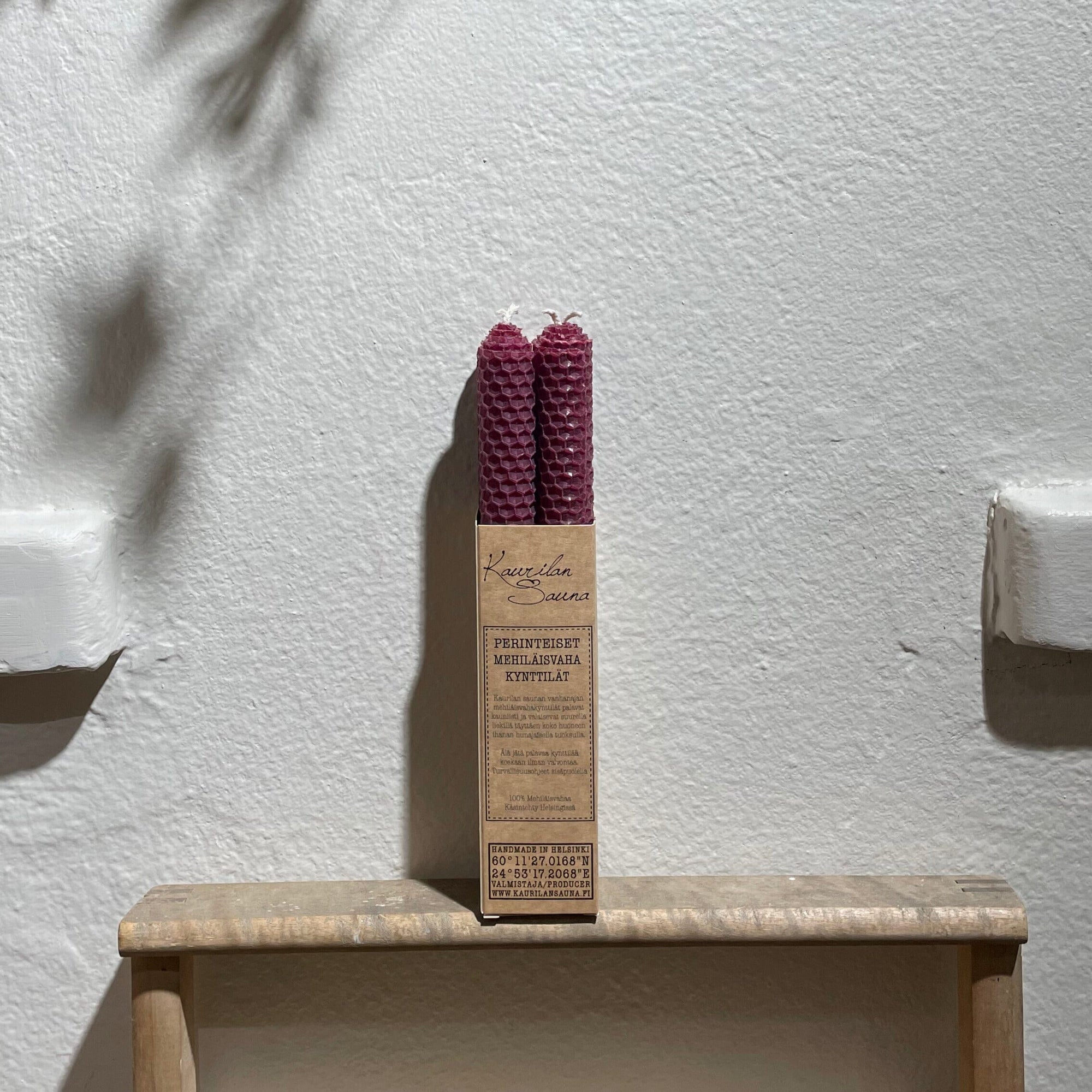 Luumunsävyiset Kaurilan Saunan mehiläisvahakynttilät 4 kpl pakkauksessa valkoista seinää vasten.