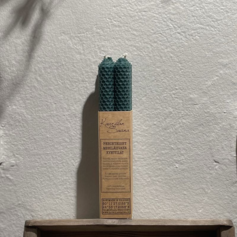 Kaurilan Saunan metsänvihreät mehiläisvahakynttilät 4 kpl pakkauksessa valkoista seinää vasten.