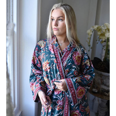 Powell Craftin puuvillainen kimono-aamutakki, jossa männynvihreällä pohjalla punaisen-, pinkin- ja sinapinsäyisiä block print -kuvioita ikkunasta ulos katsovan naisen yllä.