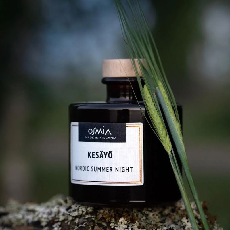Osmian Kesäyö-huonetuoksun tyylikäs ruskea lasipullo hämyisessä kesäyössä.