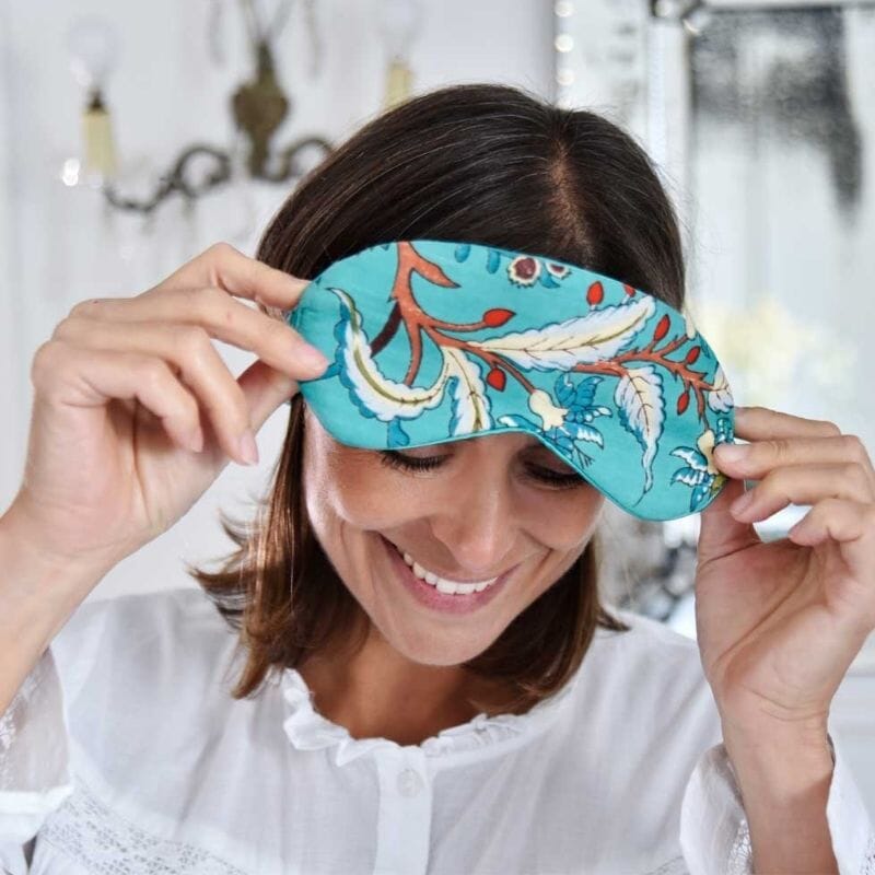 Powell Crafrt Teal Exotic Flower Print -unimaski tummahiuksisen, valkoiseen yömekkoon pukeutuneen naisen otsalla.