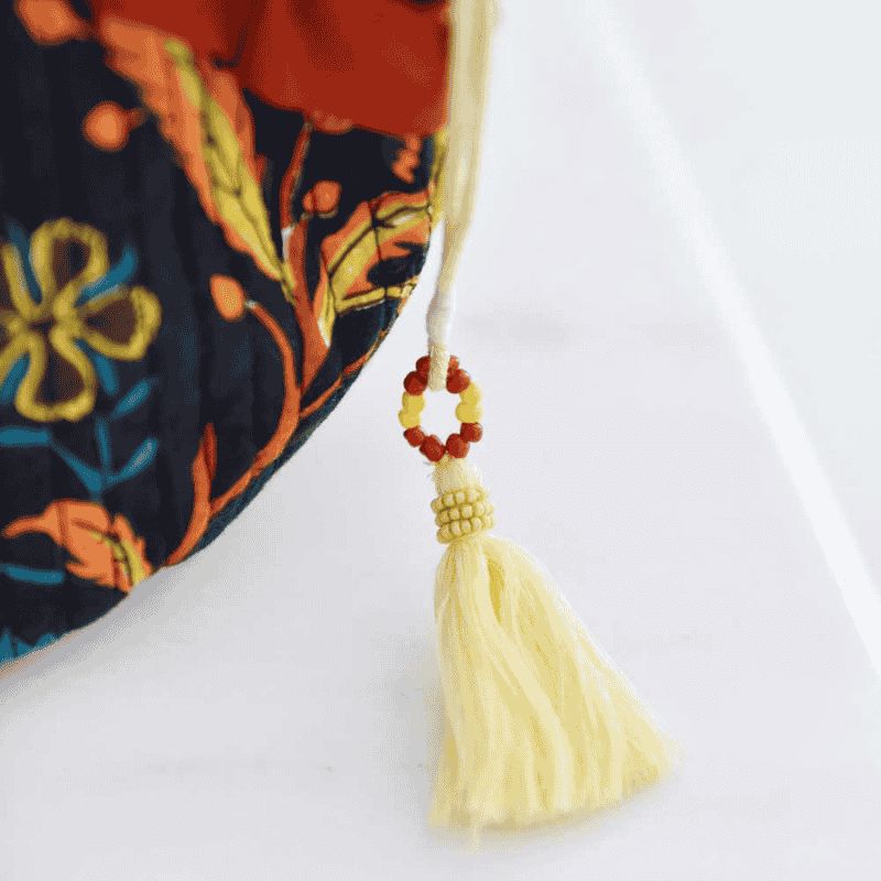 Lähi kuva toilettilaukun yksityiskohdasta. Kuvassa näkyy sitruunankeltainen vetoketjun tupsukoriste, punaisin ja keltaisin helmin.