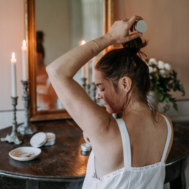 Kaurilan Saunan Saara levittämässä deovoidetta kainaloonsa mehiläisvahakynttilöiden valossa.