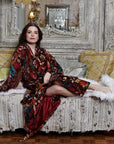 Powell Craft Velvet burgundy floral naisten puuvillainen kimono-aamutakki antiikkisen sohvalla sivuttain istuvan tummahiuksisen naisen yllä. 