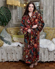 Powell Craft Velvet burgundy floral naisten puuvillainen kimono-aamutakki antiikkisen sohvan edessä seisovan tummahiuksisen naisen yllä. 