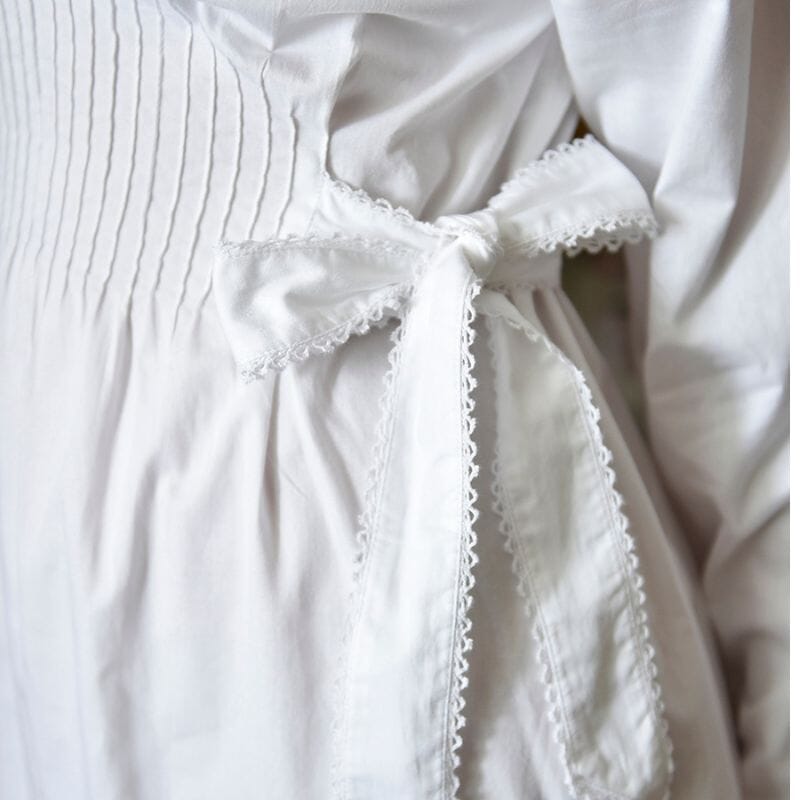 Yksityiskohta Powell Craftin Virginia-yöpaidasta. Pitsireunainen nauha, jolla yöpaidan leveyttä voi säätää vyötäröltä, on sidottu kauniille rusetille.