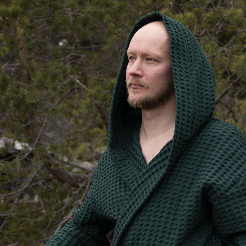 Metsänvihreään Keltainen designin vohvelikylpytakkiin pukeutunut mies mietteliäänä metsässä.