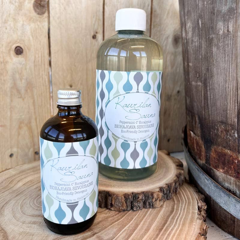 Kaurilan saunan Biohajoava siivousaine 500 ml  kirkkaassa muovipullossa ja 100ml ruskeassa lasipullossa puisilla korokkeilla.