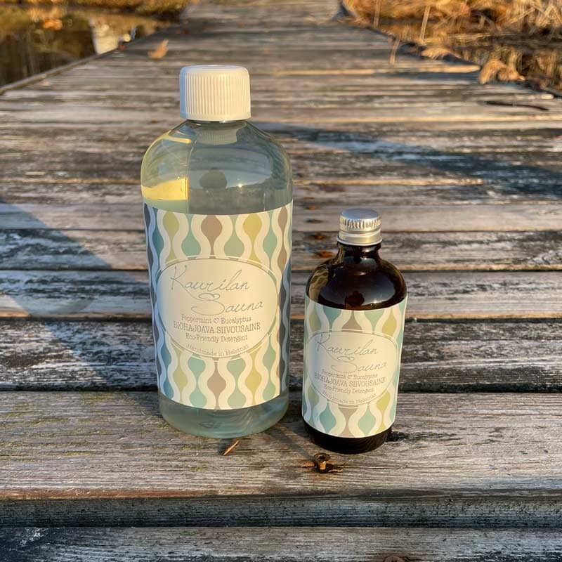 Kaurilan saunan Biohajoava siivousaine 500 ml  kirkkaassa muovipullossa ja 100ml ruskeassa lasipullossa syksyisellä laiturilla.