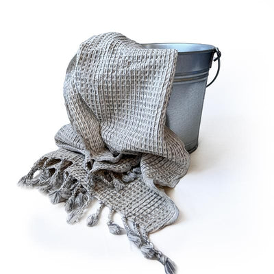 Saunatonttu by Kaurilan saunan harmaa-valkoinen Eliaksen Hamam -vohvelipyyheliina, jonka päissä puolikierrehapsut.