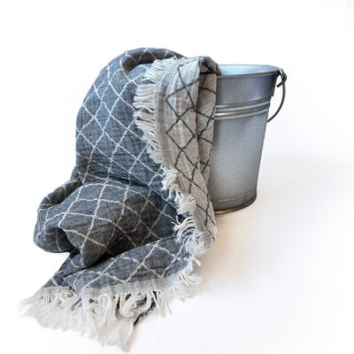 Saunatonttu by Kaurilan saunan Ellenin Hamam-pyyheliina sävyssä Kaarna, jossa toisella puolella harmaalla pohjalla valkoinen ristikkokuvio ja toisella päinvastainen, sekä päissä kevyet pienet hapsut.