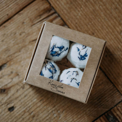 Ikkunallisessa pahvirasiassa näkyy neljä Kaurilan Saunan valkoista sinisillä kukan terälehdillä koristeltua eukalyptus jalkakylpytablettia. 