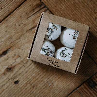 Ikkunallisessa pahvirasiassa näkyy neljä Kaurilan Saunan valkoista laventelin kuivatuilla kukilla koristeltua laventeli jalkakylpytablettia. 