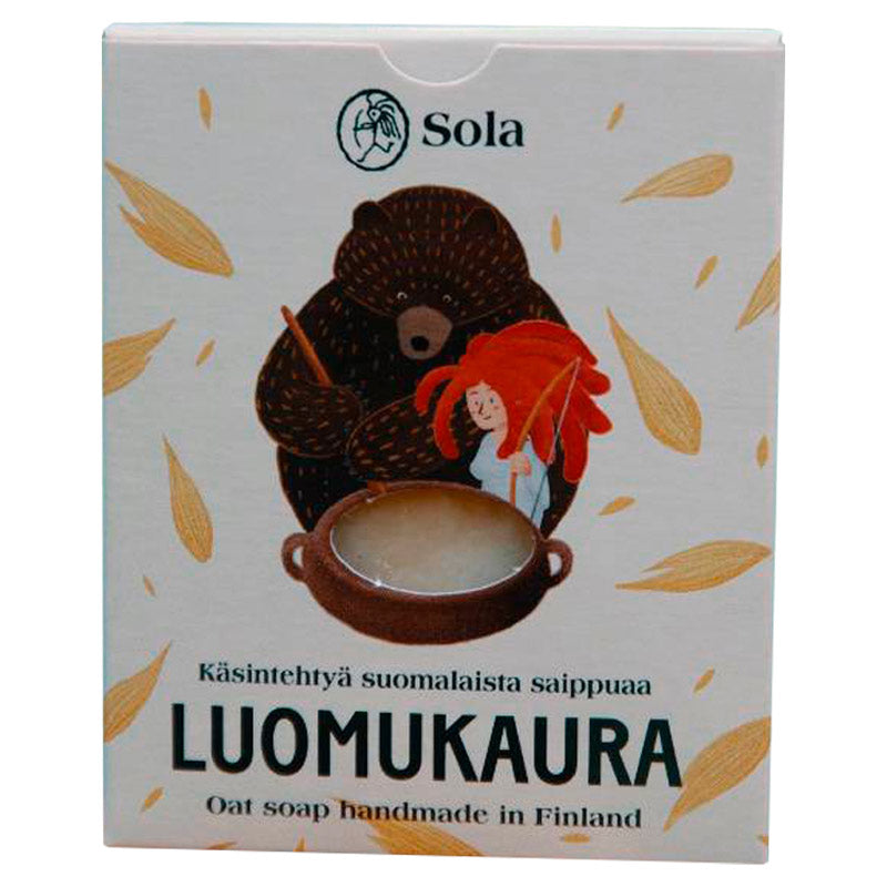 Solan Luomukaura -saippua suloisess vaaleanharmaassa pahvipakkaksessa, jota koristavat piirretyt kauranjyvät sekä saippuapataa sekoittavat karhu ja punahiuksinen tyttö.