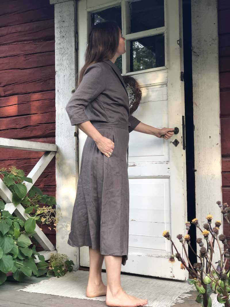 Saunatonttu Saaran Pellava-aamutakki  sävyssä kahvi Kaurilan saunan ovella seisovan Saunatonttu Saaran yllä. 