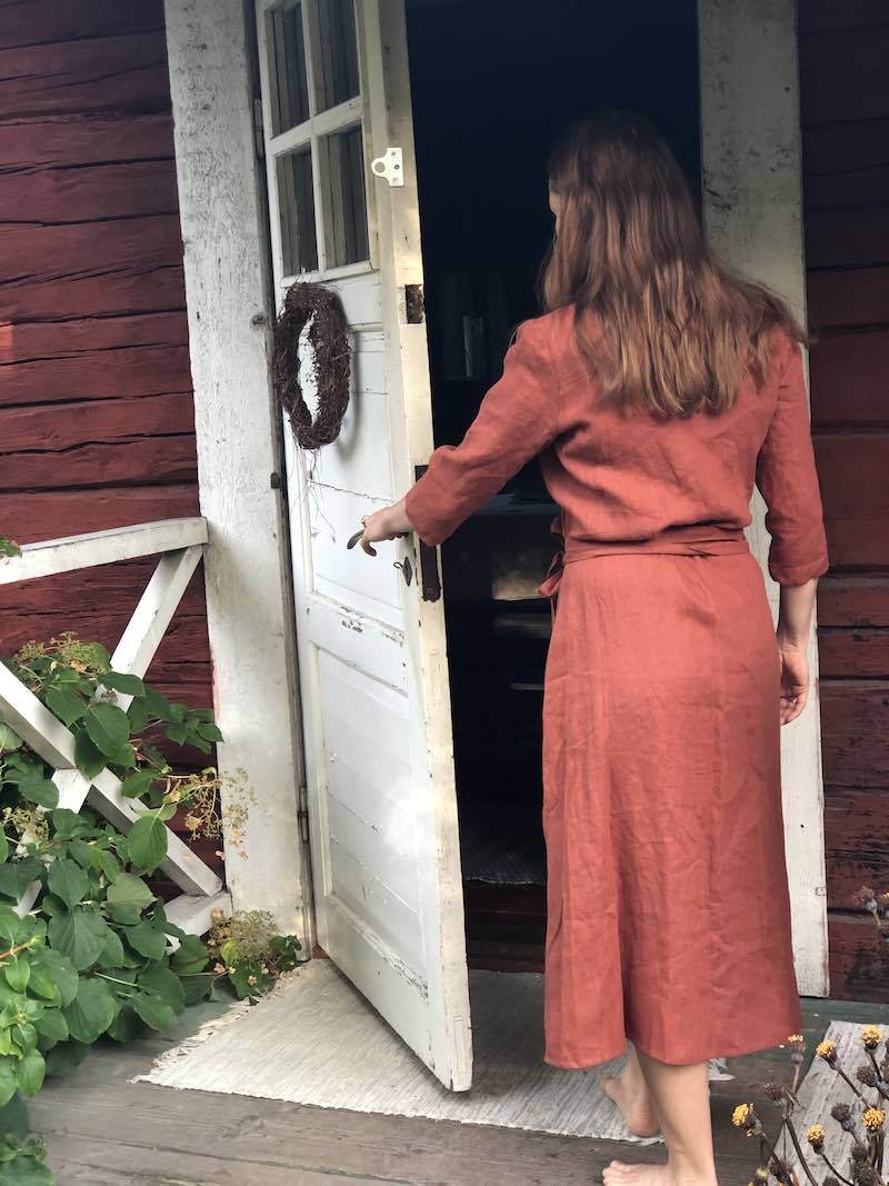 Saunatonttu Saaran Pellava-aamutakkiin  sävyssä 'Ruoste' pukeutunut Saunatonttu Saara astumassa Kaurilan saunan ovesta sisään. 