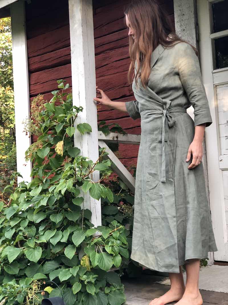 Saunatonttu Saaran Pellava-aamutakkiin sävyssä salvia pukeutunut Saunatonttu Saara seisomassa Kaurilan saunan kuistilla.