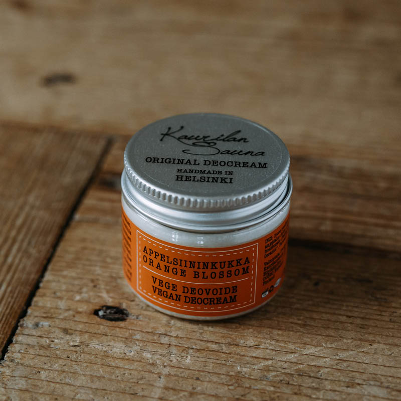 Kaurilan Saunan vegaaninen appelsiininkukilta tuoksuva deovoide oranssissa kierrekorkillisessa muovipurkissa, puisella pöydällä.
