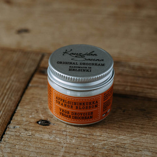Kaurilan Saunan vegaaninen appelsiininkukilta tuoksuva deovoide oranssissa kierrekorkillisessa muovipurkissa, puisella pöydällä.
